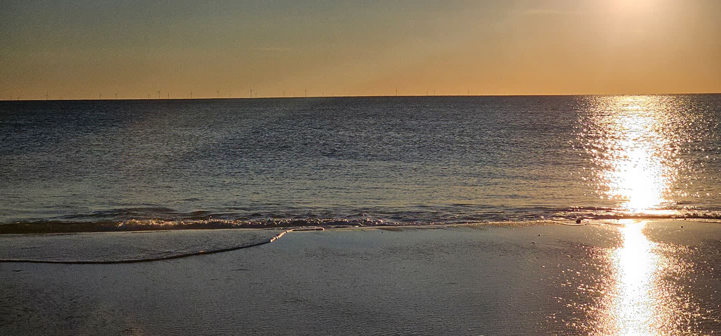 Low sun over open water off Martha's Vineyard, its reflection running back across the wet sand at the tide line